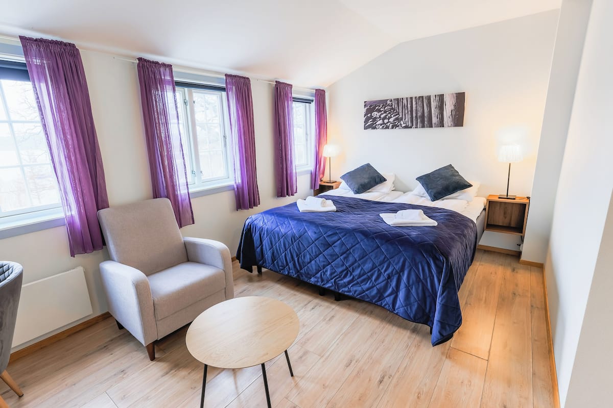 Ein Hotelzimmer mit Bett, Sessel, rundem Tisch und zwei Nachttischlampen.