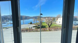 A view through a window of a marina with boats, a lake, and a grassy area with a building. - Verkshotellet (Strand)