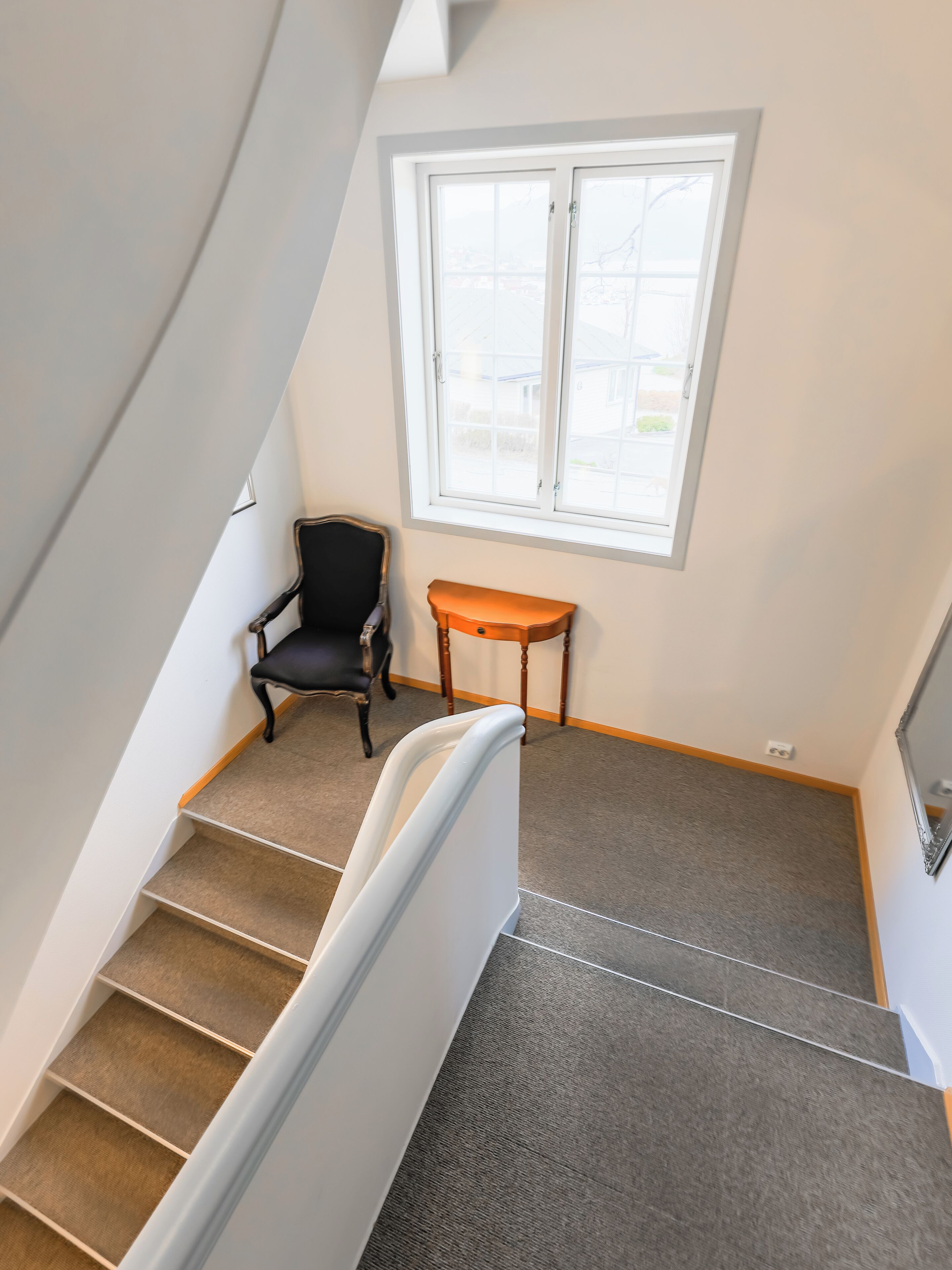 Eine Treppe mit Teppichstufen, ein schwarzer Stuhl, ein Holztisch und ein Fenster mit Blick ins Freie.
