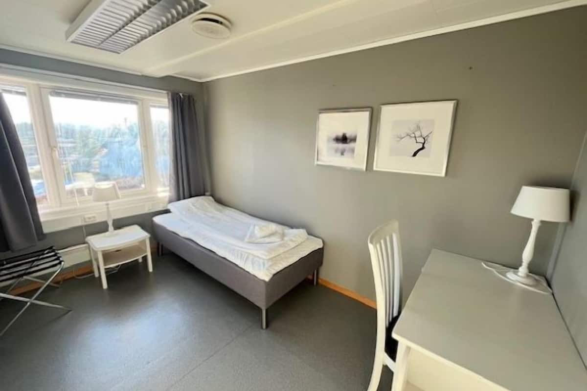 Ein kleines, ordentlich eingerichtetes Schlafzimmer mit einem Bett, einem Schreibtisch, einem Stuhl und zwei gerahmten Bildern an der Wand.