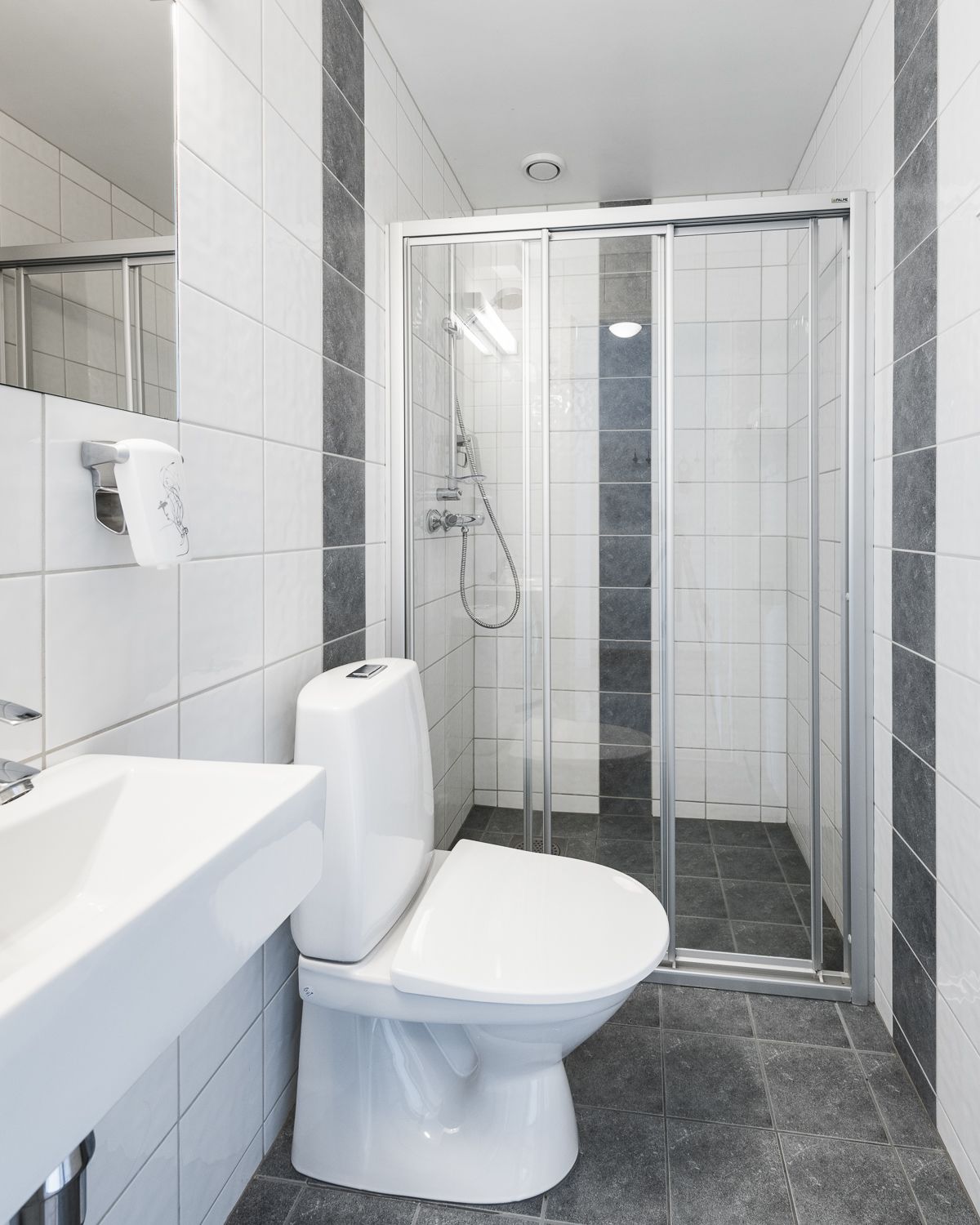 Et moderne badeværelse med toilet i hvidt, brusekabine i glas og håndvask i hvid.
