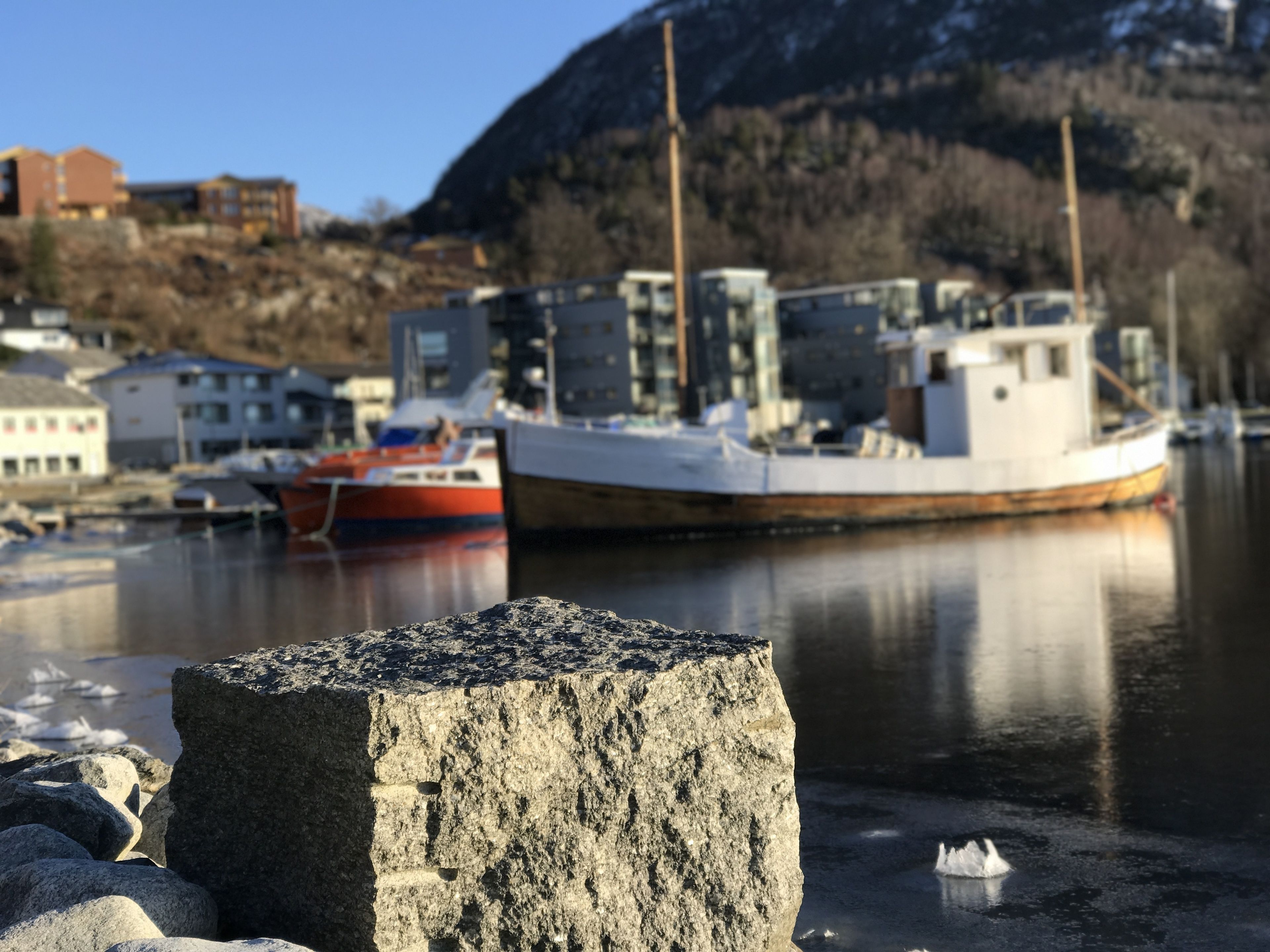 Ein Hafen mit Booten, ein großer Felsen im Vordergrund und Gebäude im Hintergrund.