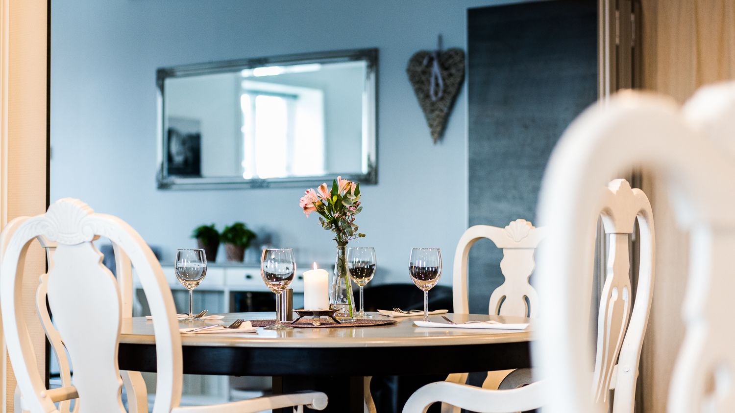 A dining table with white chairs, a vase with flowers, and wine glasses.