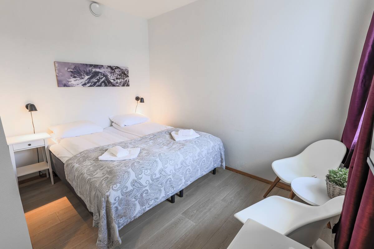 Ein Schlafzimmer mit einem Bett, Nachttischen, einem Sessel, einer Wandlampe und einem Gemälde.