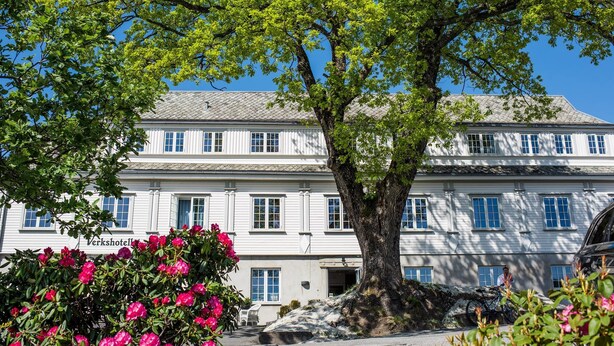 A large white building with multiple windows and a tree in front. - Verkshotellet (Strand)
