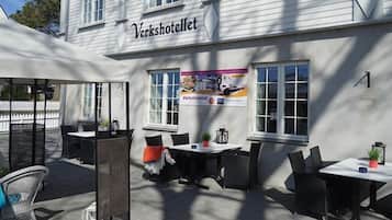 An outdoor seating area with tables and chairs, a sign reading "Verkshotellet", and a banner advertising the restaurant.