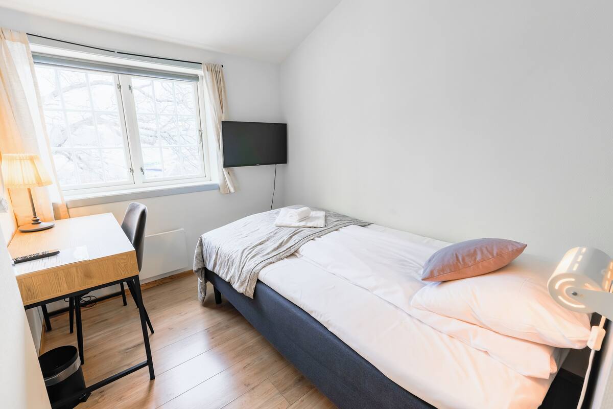Ein Schlafzimmer mit Bett, Schreibtisch, Stuhl, Fernseher und Fenster.