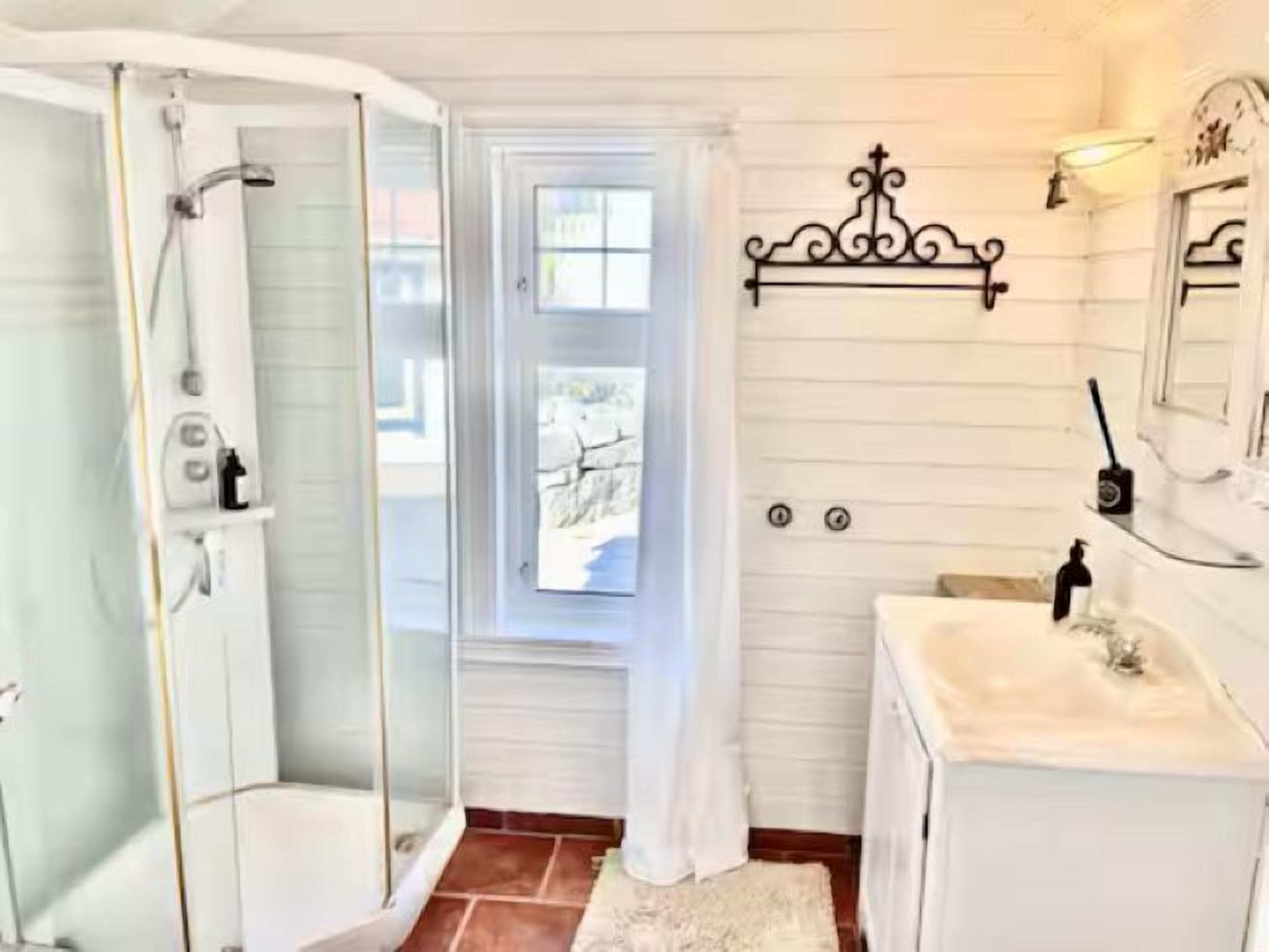 A bathroom with a glass shower enclosure, a window with a view, and a white sink with a mirror above it.