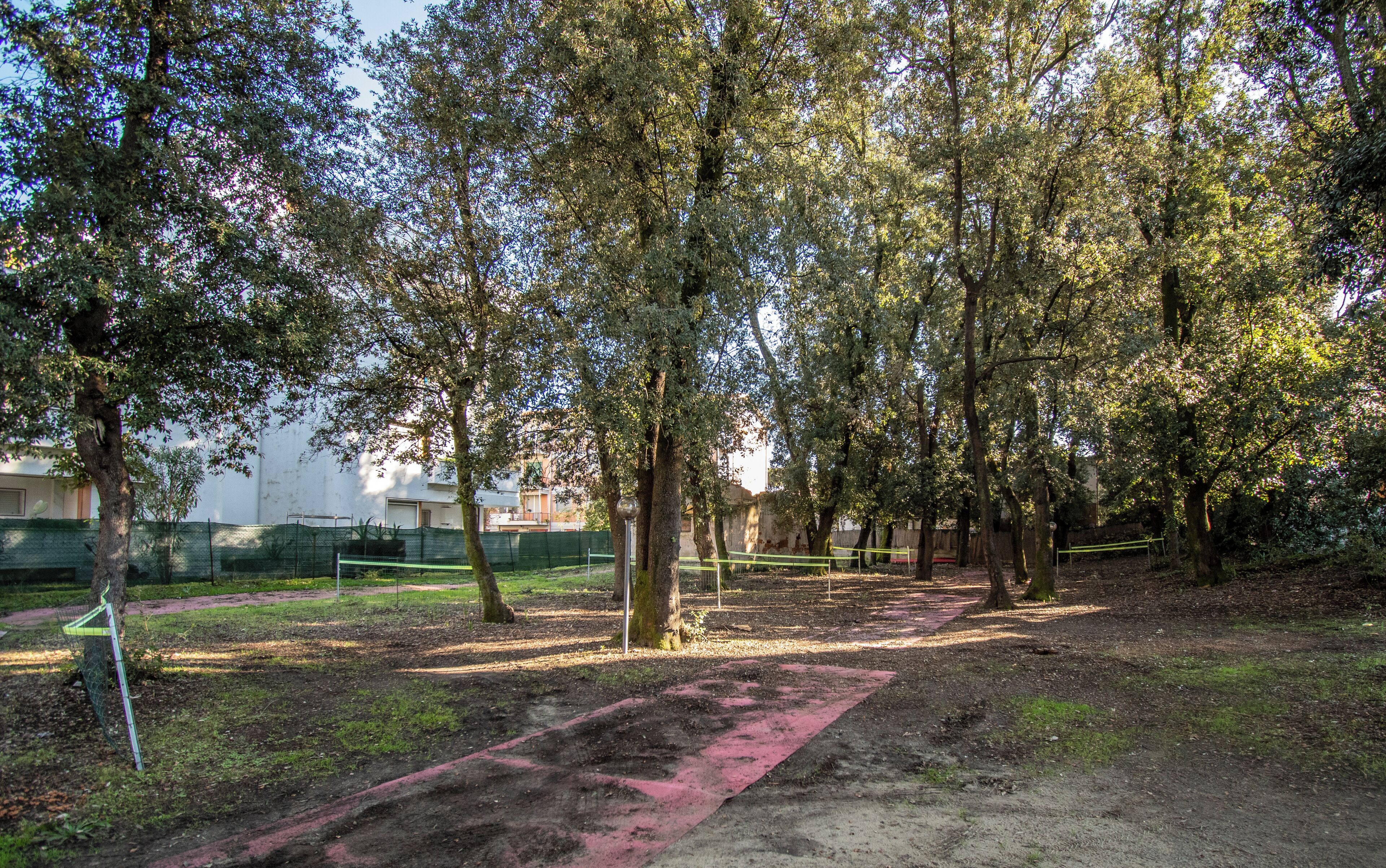 Un parque con árboles, un sendero de tierra y una valla.