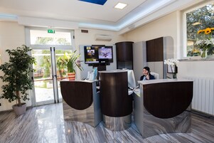 Un área de recepción de diseño moderno, con mostrador de recepción, un televisor montado en la pared y una planta en maceta.