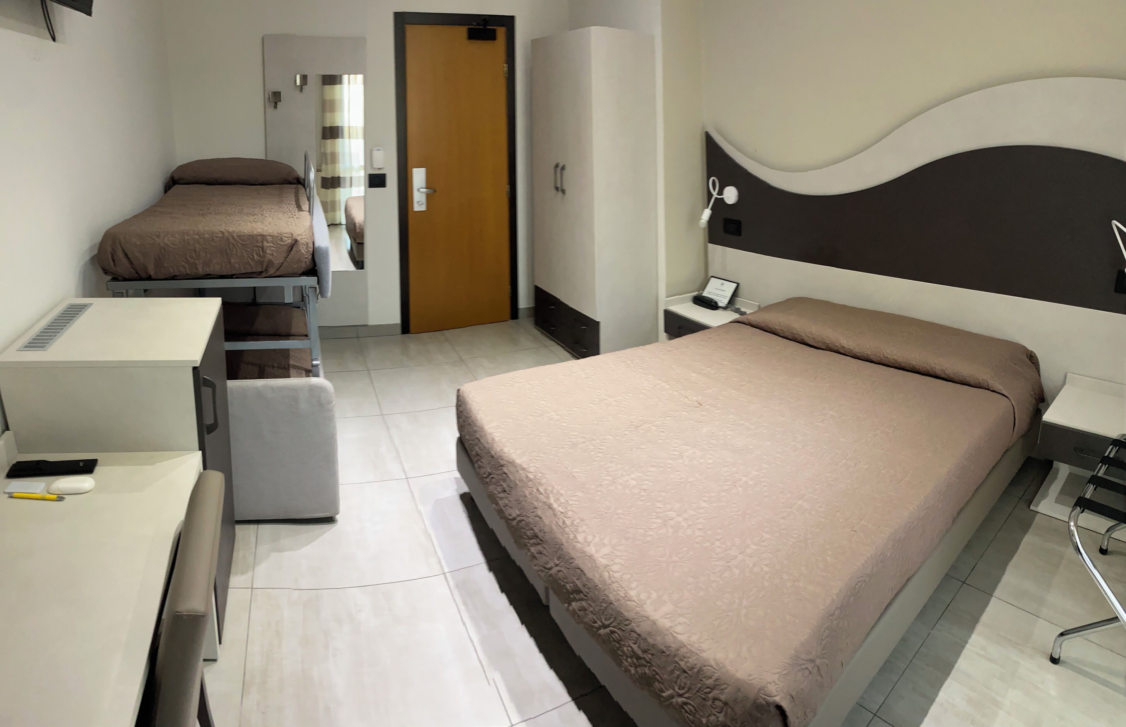 Habitación de hotel con cama, escritorio, silla, armario y puerta de baño.
