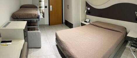 Habitación de hotel con cama, escritorio, silla, armario y puerta de baño.