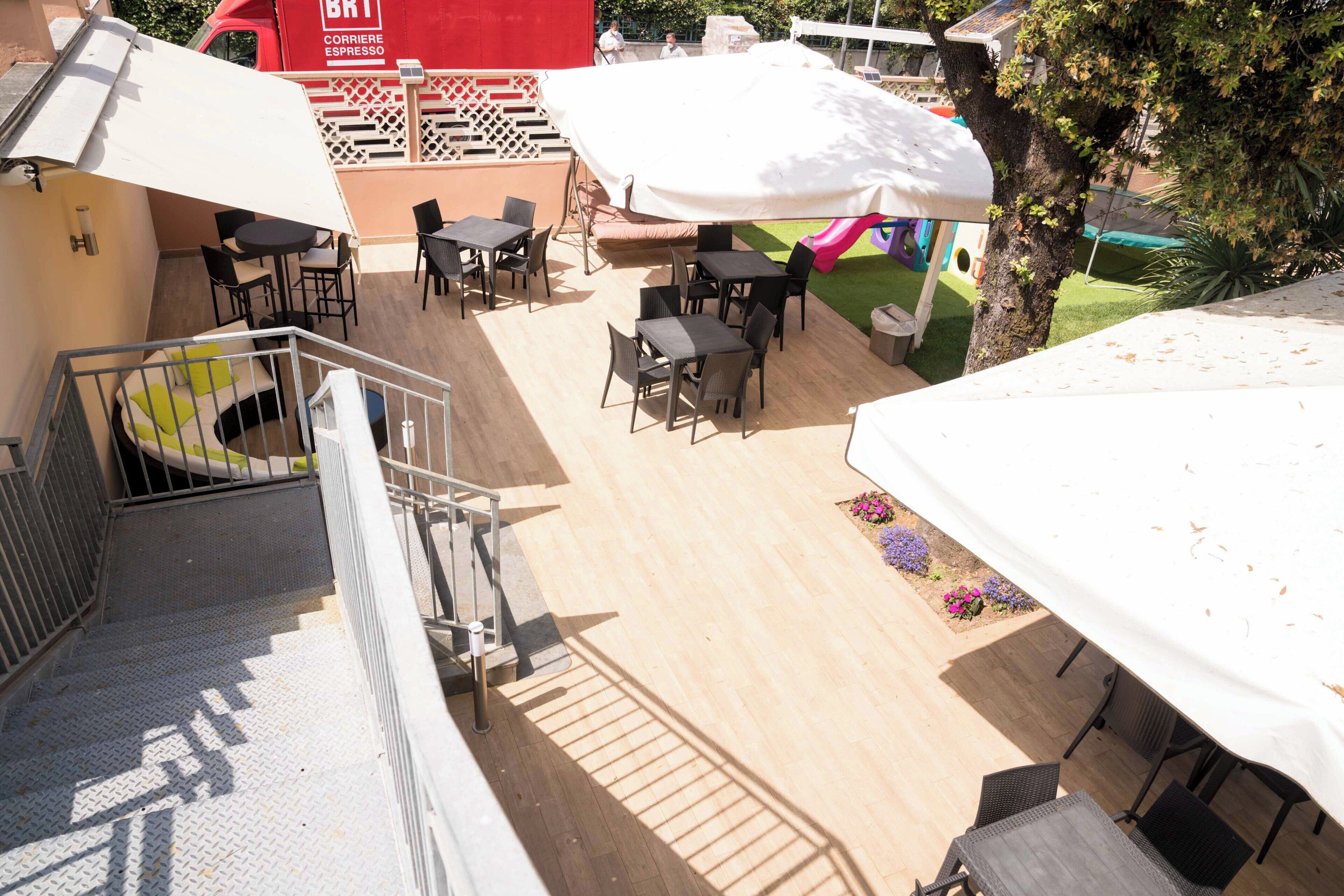An outdoor patio area with tables and chairs, a covered seating area, and a playground in the background.