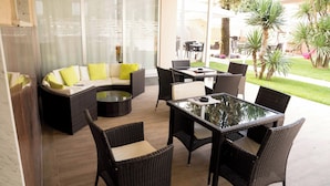 A modern outdoor seating area with wicker furniture, a glass-top table, and a curved sofa with cushions. - Hotel Roma (Massa)