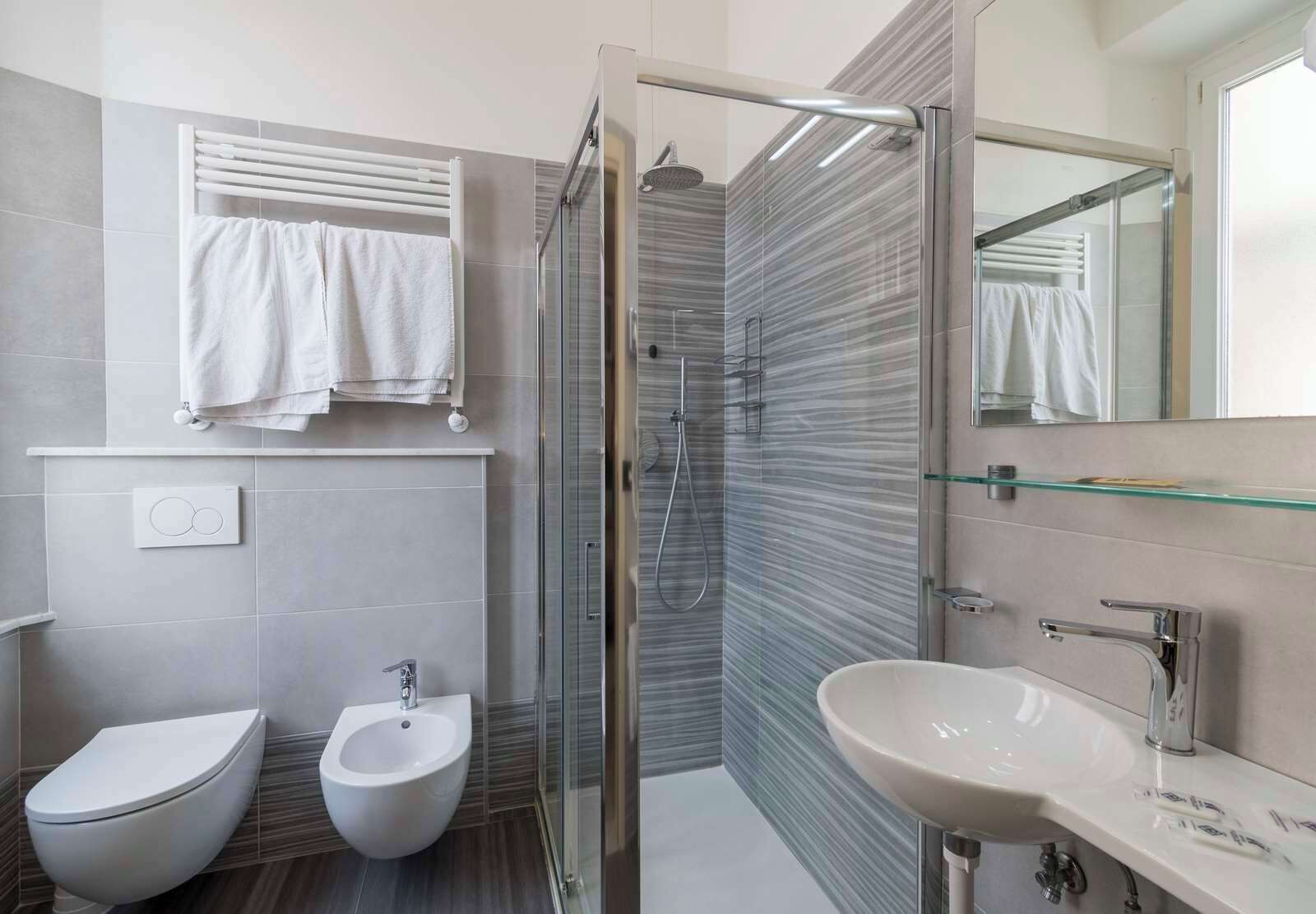 A modern bathroom with a glass-enclosed shower, a bidet, a toilet, and a sink with a mirror above.