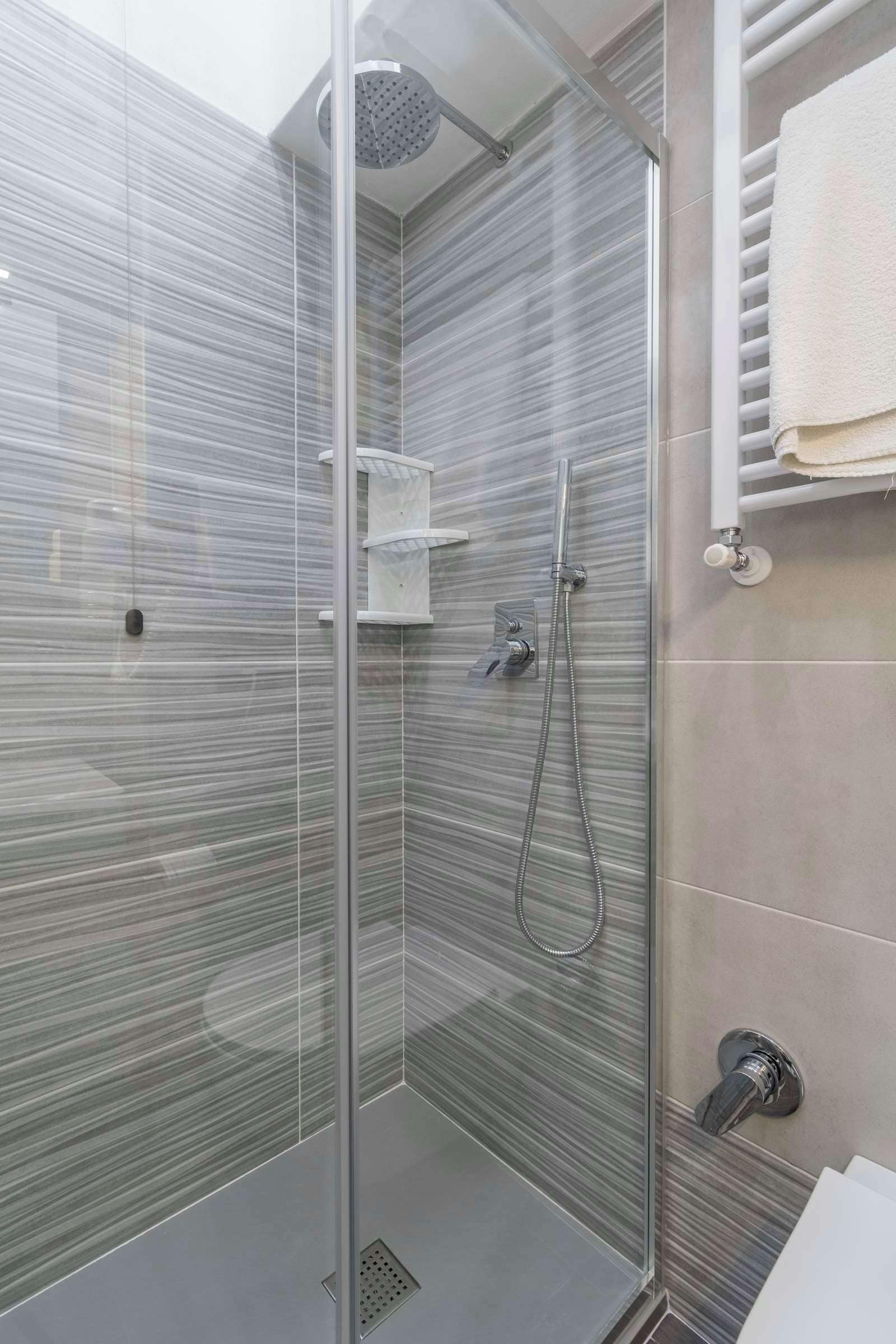 Eine moderne Dusche mit Glastür, Handbrause und einem an der Wand befestigten Handtuchhalter.