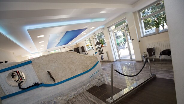 A modern interior with a large boat sculpture, a glass barrier, and a view of the outdoors. - Hotel Roma (Massa)