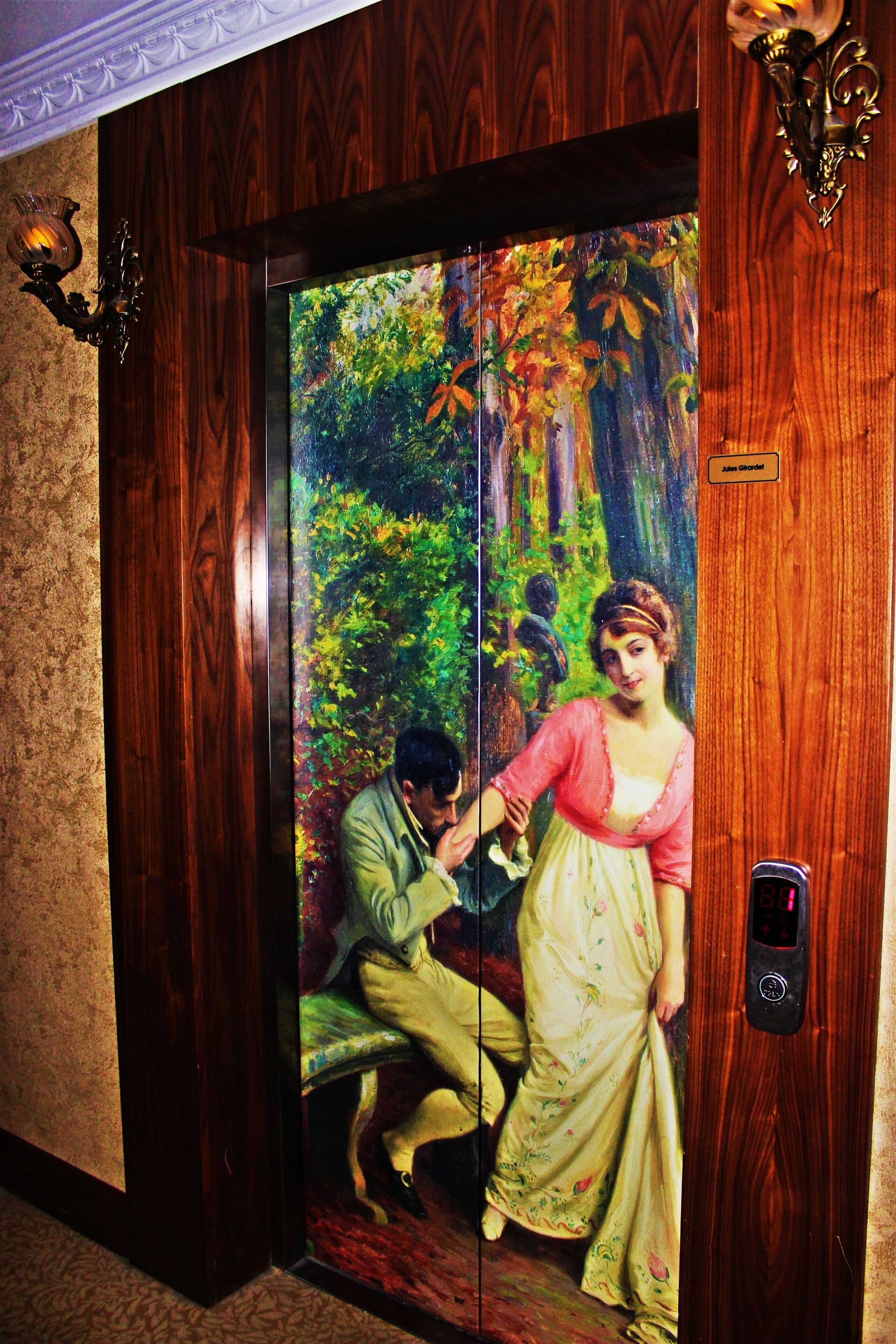 Un ascensor con un mural de una escena boscosa y una mujer con vestido.