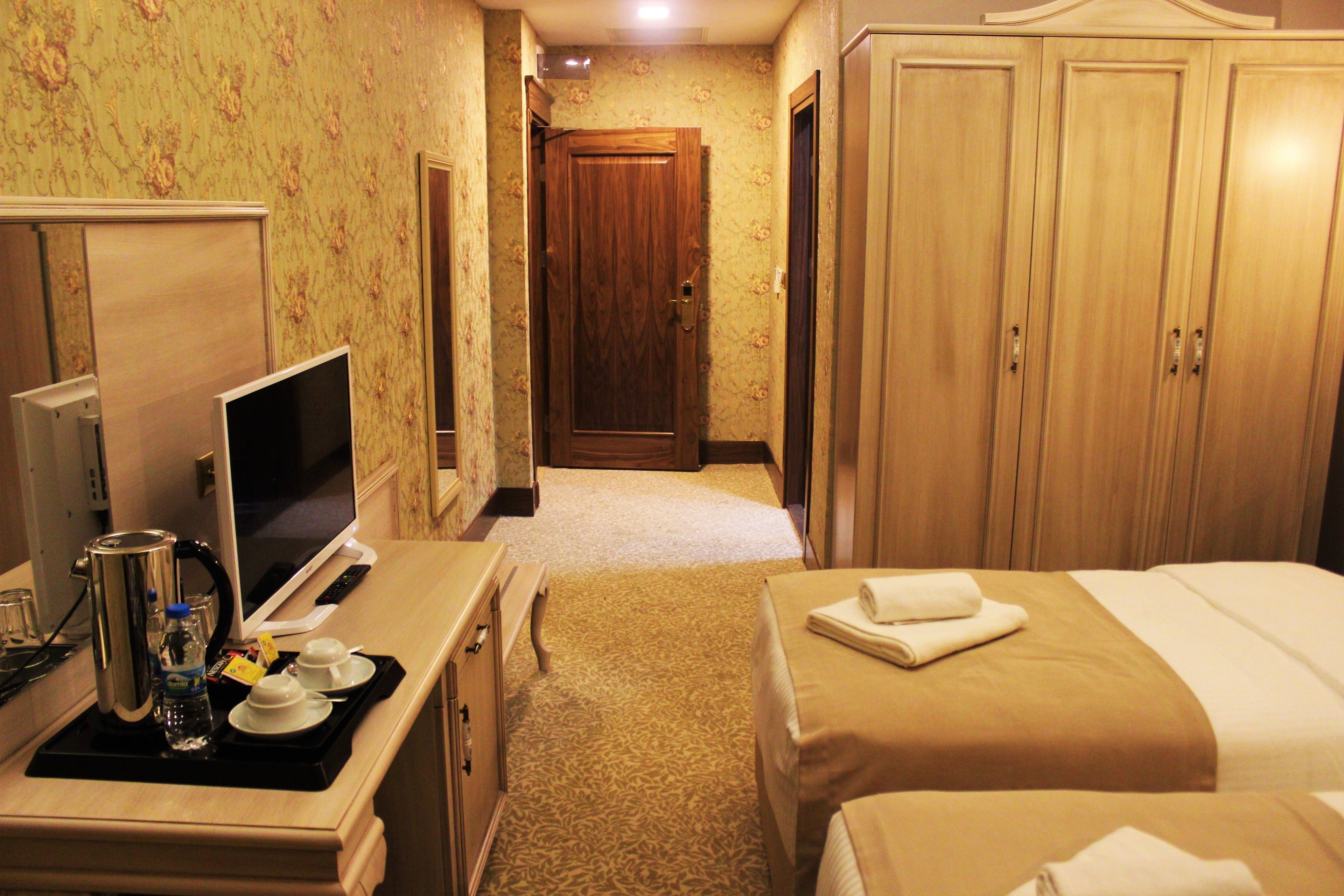 A hotel room with a bed, a desk with a computer and a coffee maker, a TV, and a wardrobe.