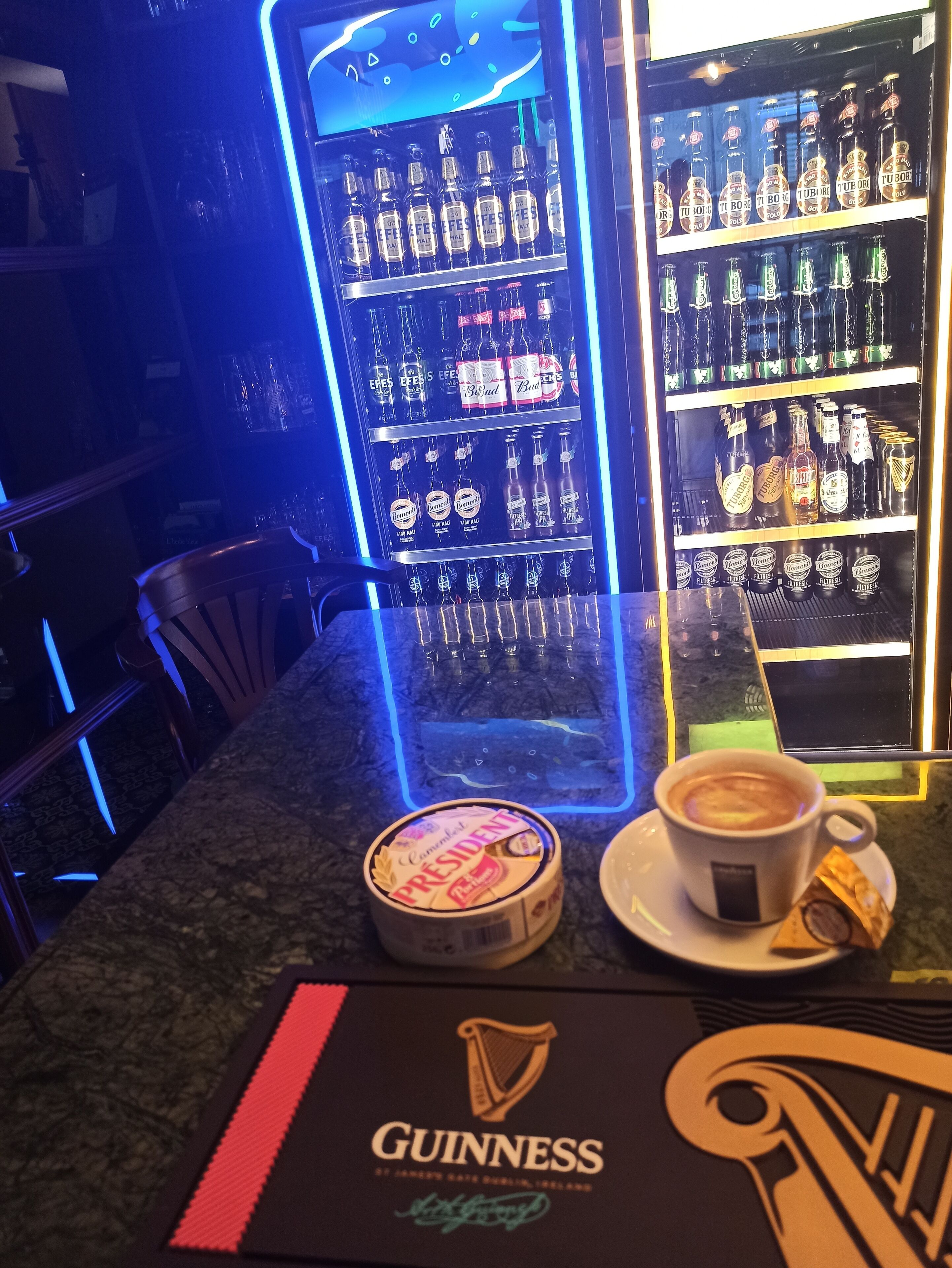 A bar area with shelves of bottled beverages, a coffee cup, and a Guinness coaster.