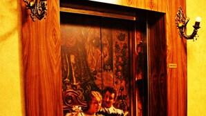Un ascensor con paneles de madera y diseño vintage, con un mural en la pared que muestra a dos personas.