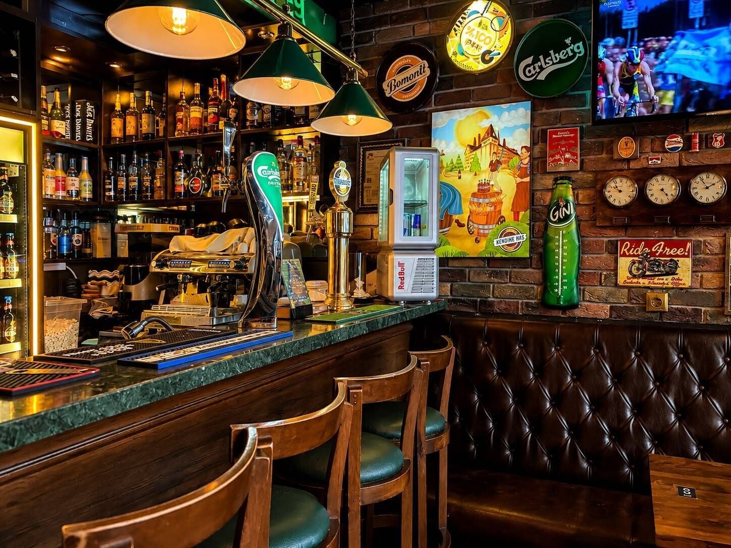 A bar area with a counter, bar stools, a coffee machine, and a variety of bottles and glasses.