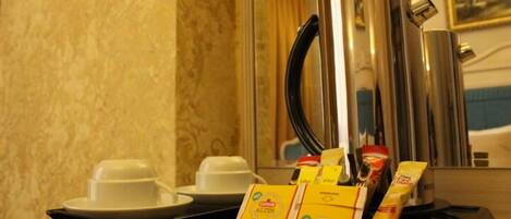 Habitación de hotel con minibar que contiene una cafetera, una bandeja con tazas y aderezos, y un espejo que refleja la decoración de la habitación.