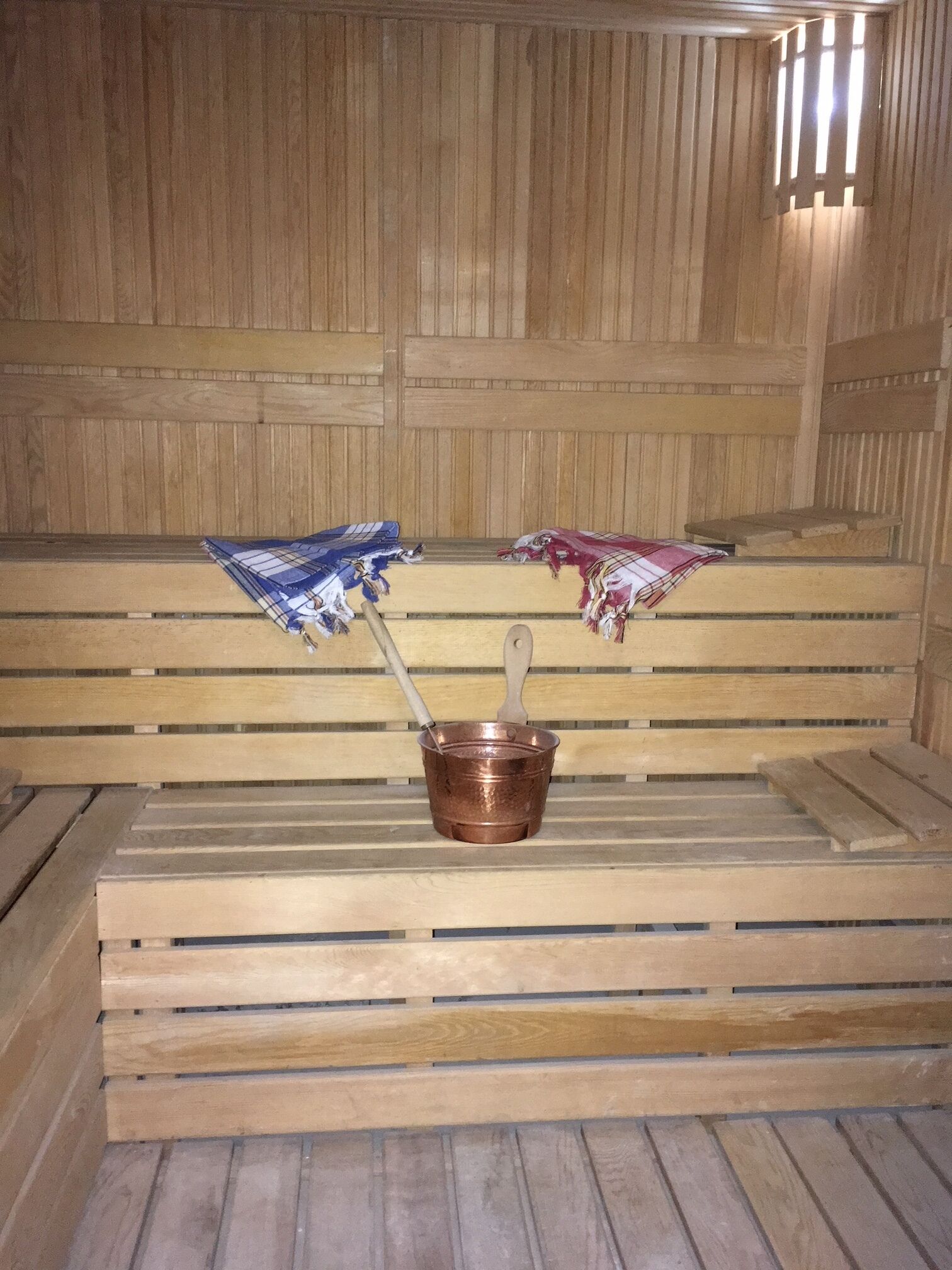 A wooden sauna bench with a copper bucket and two towels.