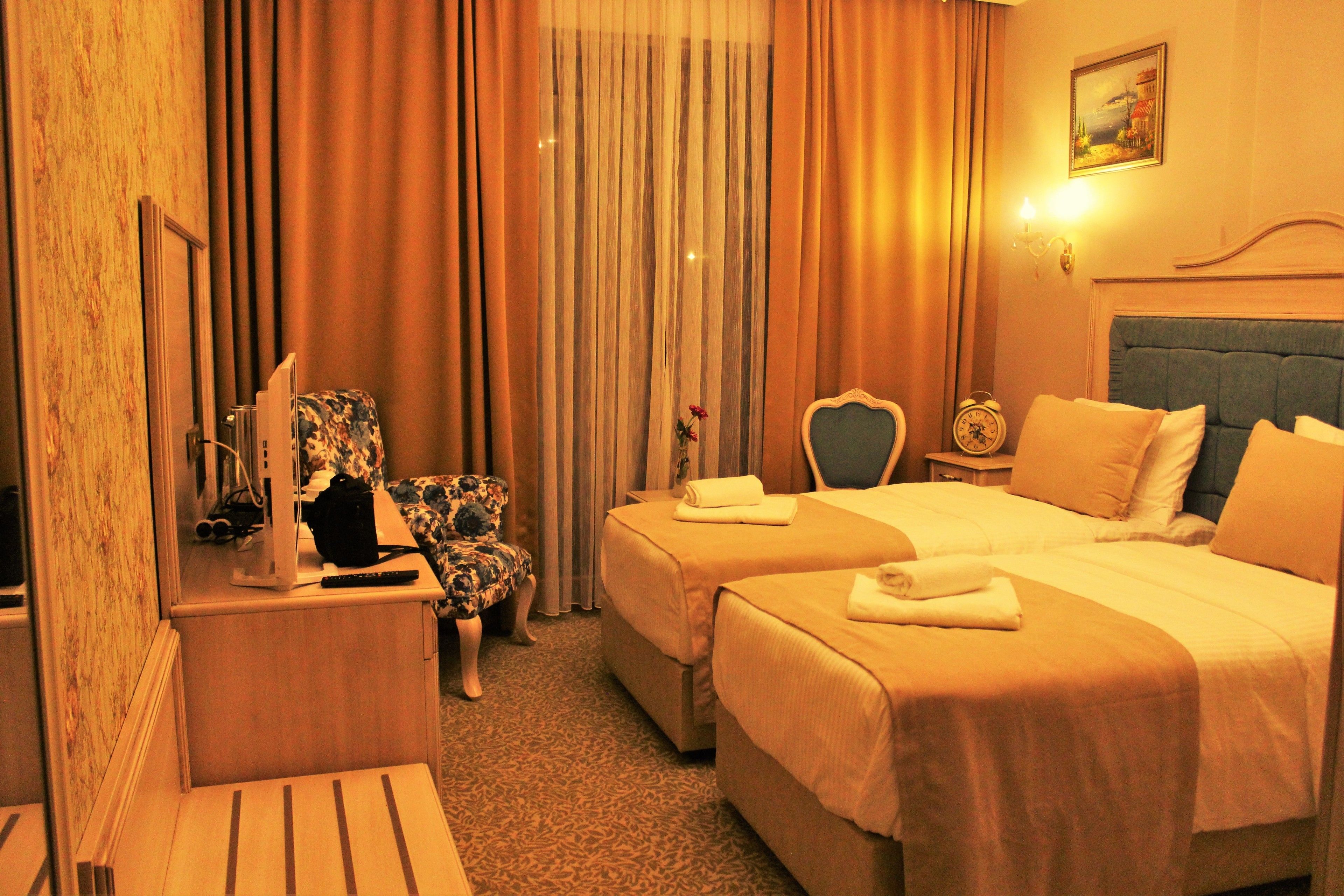 A hotel room with two beds, a desk, a chair, and a painting on the wall.