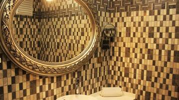 A bathroom with a checkered tile wall, a round mirror with an ornate frame, a sink, and a towel on the counter.