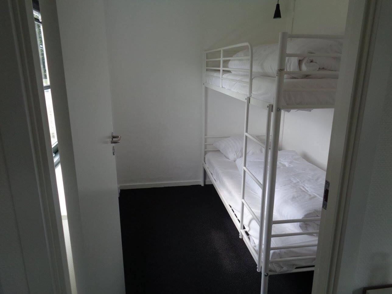 Een kleine, smalle kamer met een stapelbed en een deur naar een andere kamer.