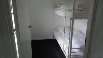 Een kleine, smalle kamer met een stapelbed en een deur naar een andere kamer.