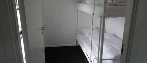 A small, narrow room with a bunk bed and a door leading to another room.
