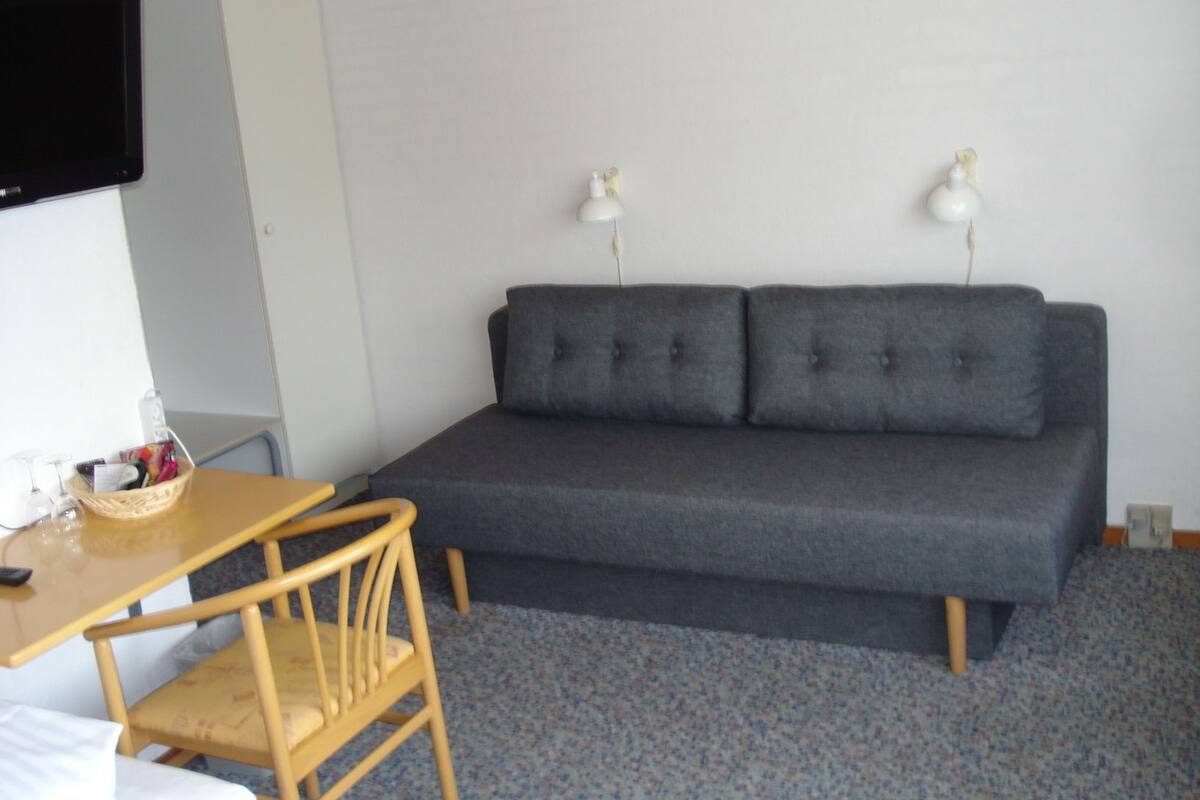 Et værelse med en grå sofa, en træstol, et lille bord med en kurv, og to væglamper.