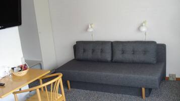Una habitación con un sofá gris, una silla de madera, una mesita con una cesta y dos lámparas fijadas a la pared.