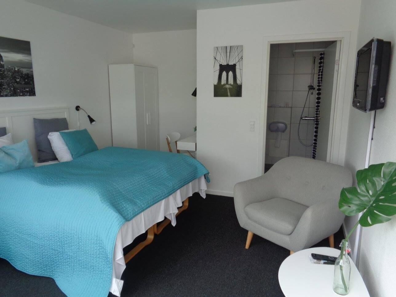A bedroom with a bed, a chair, a small table, a TV, and a shower area.
