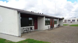 Un edificio con un patio cubierto, mobiliario exterior y un garaje al fondo.