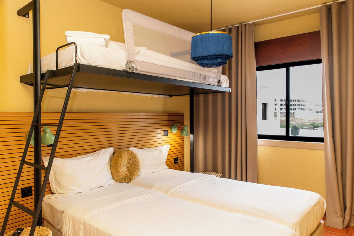 A bunk bed with a ladder, a bedside table with a lamp, and a window with curtains.