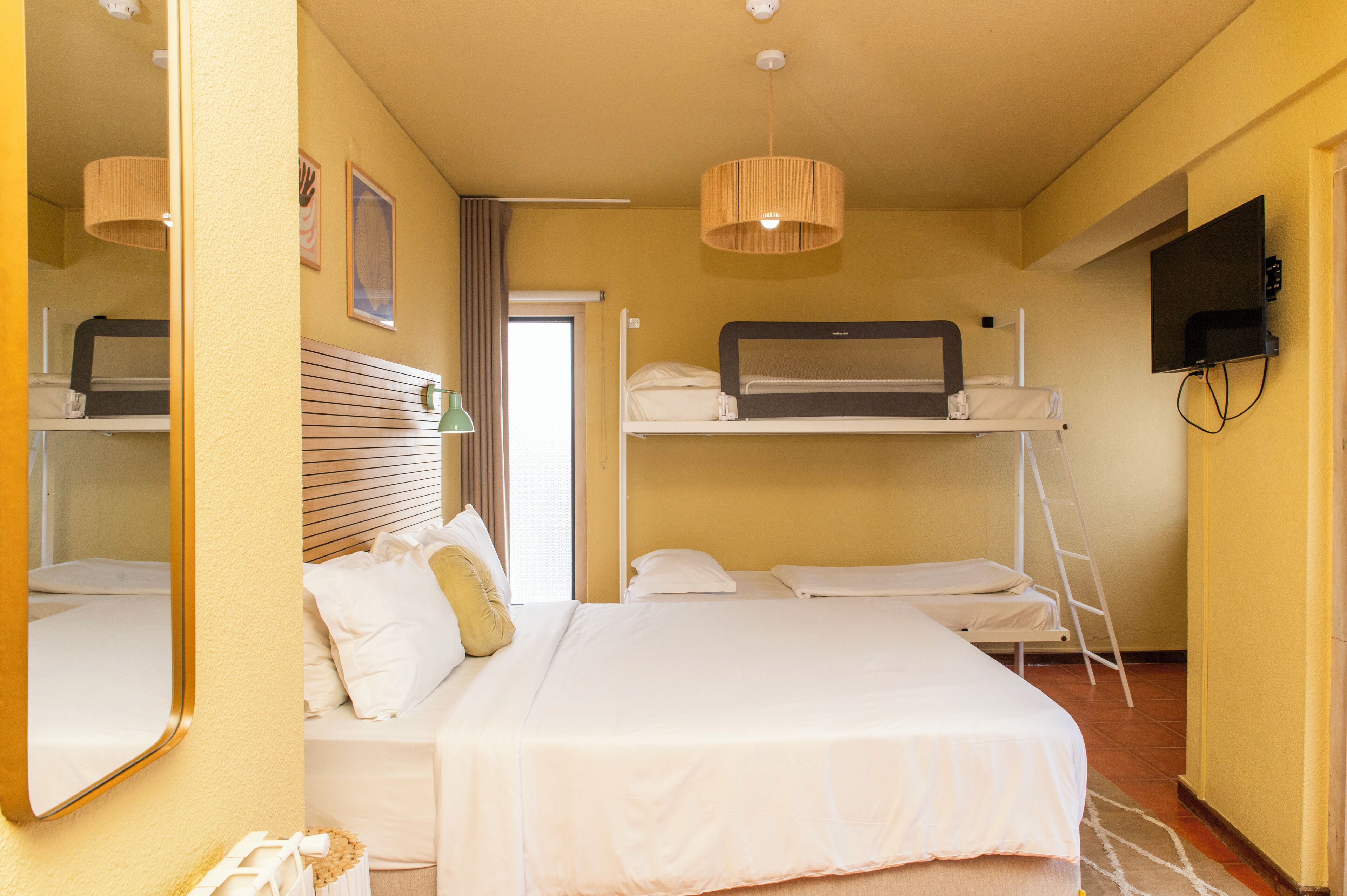 Habitación de hotel con literas, televisor de pantalla plana, espejo y ventana con cortinas.