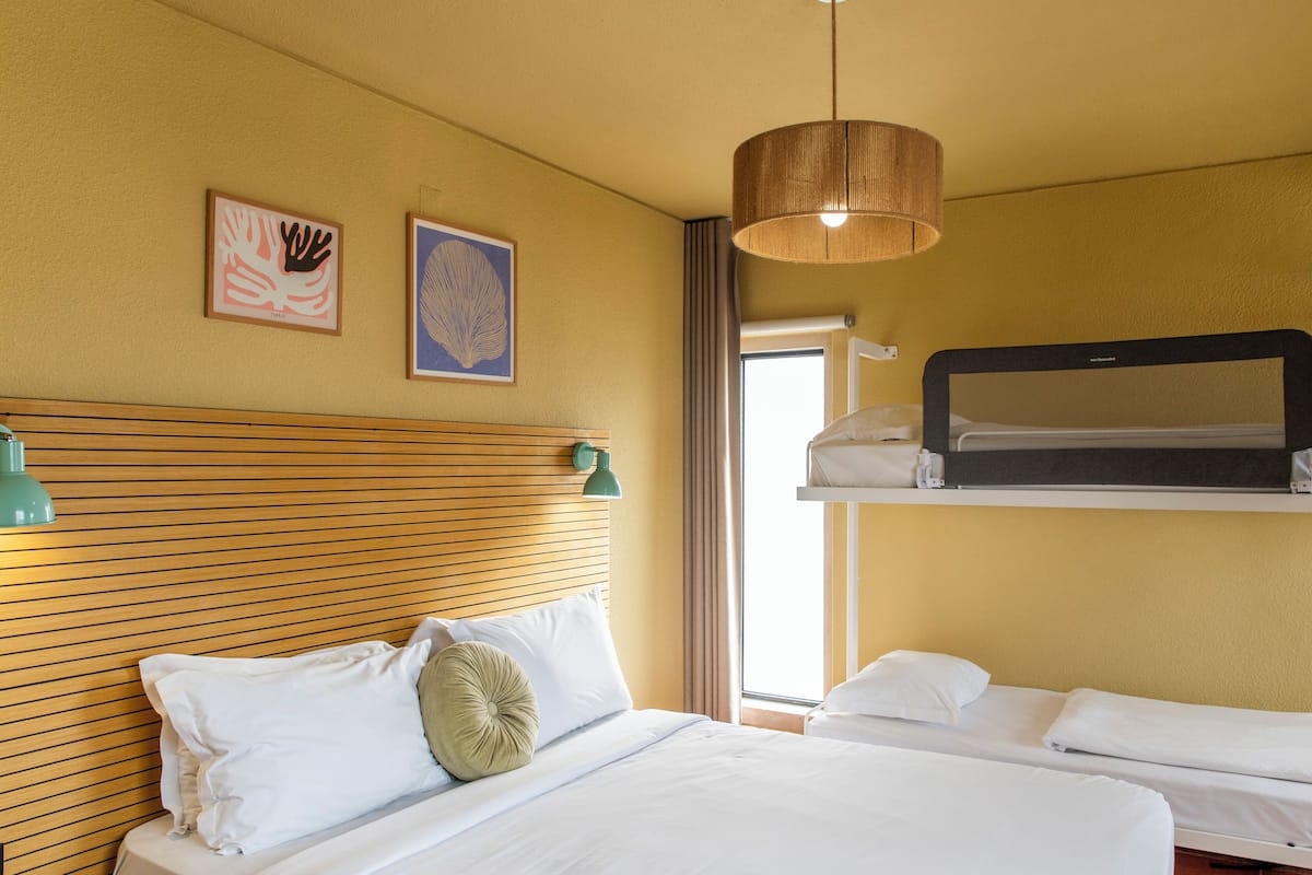 A hotel room with a wooden headboard, two beds, a hanging light fixture, and artwork on the wall.
