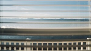 A view through window blinds of a calm body of water with distant landforms. - Auberge sur mer (Notre-Dame-du-Portage)