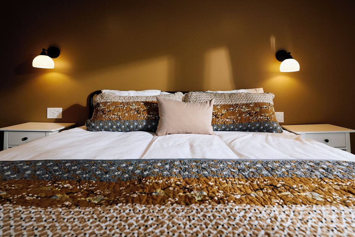 A neatly made bed with patterned bedding, two bedside lamps, and a wall socket.