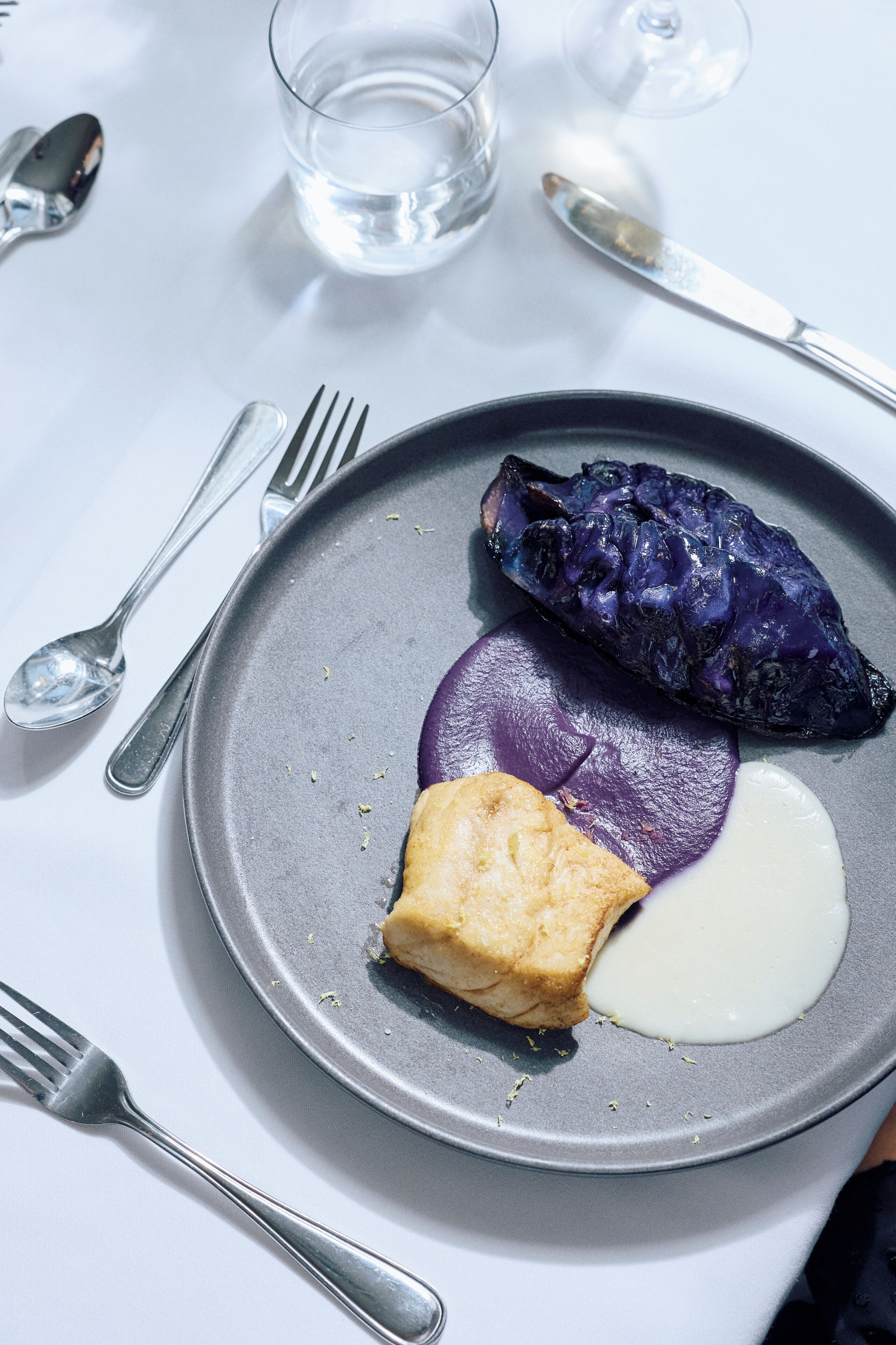 A plate with food items, a glass of water, and cutlery on a table.