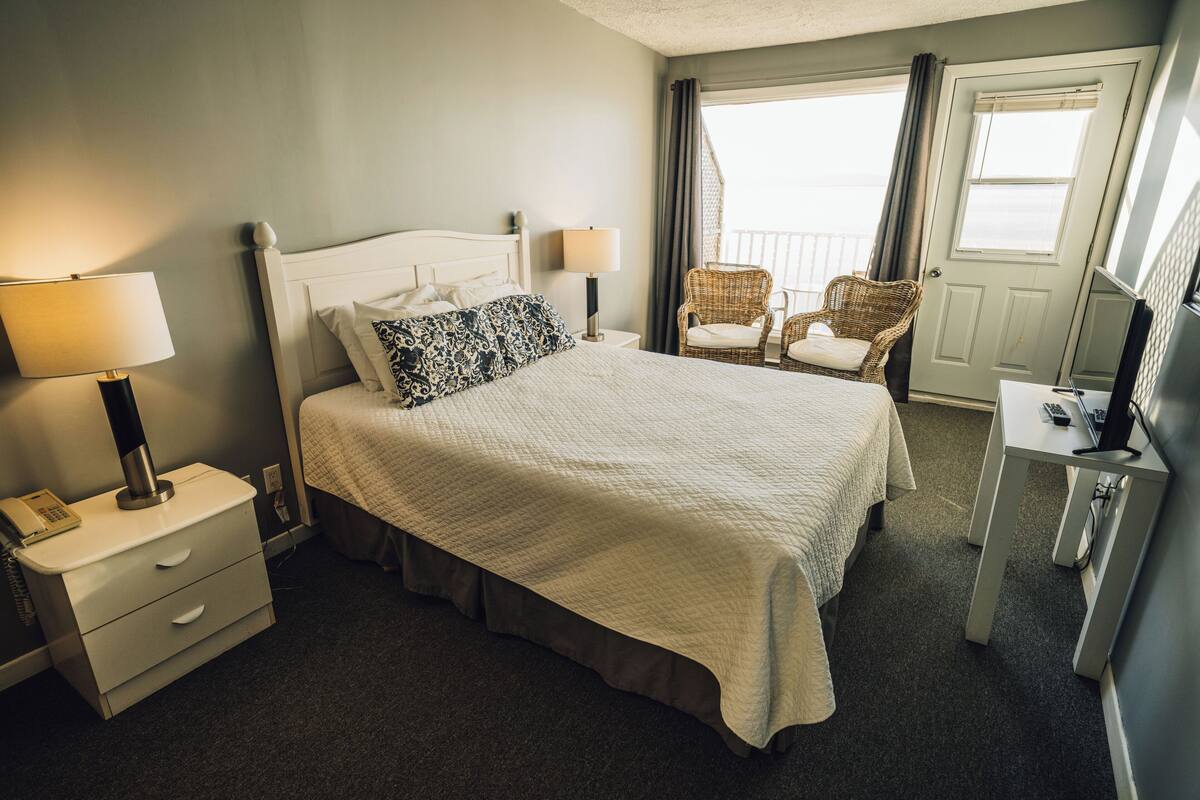A hotel room with a bed, two bedside tables, a chair, a desk, and a door.