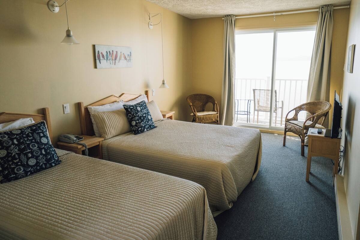 A hotel room with two beds, a chair, a desk, and a balcony.