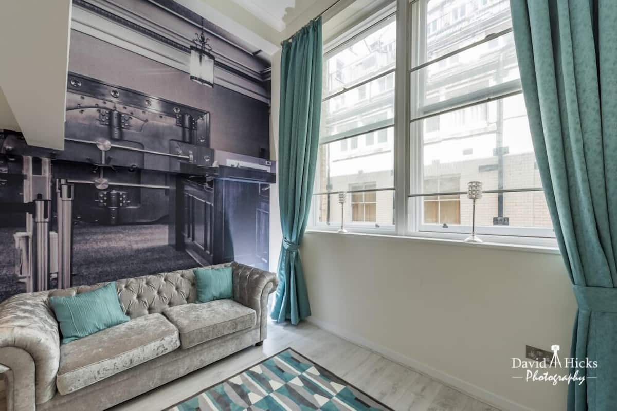 A living room with a sofa, a patterned rug, and a window with curtains.