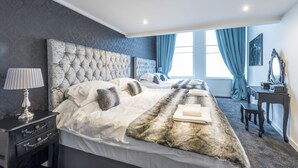 Une chambre avec deux lits, une table de chevet avec une lampe, un bureau avec un miroir et une vue sur l’extérieur grâce à de grandes fenêtres.