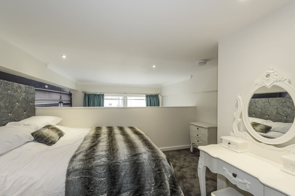A bedroom with a bed, a dresser, a mirror, and a window.