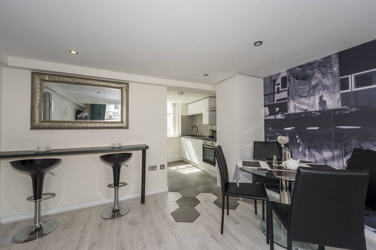 A modern kitchen with a dining area, a large mirror, and a view of the kitchen through the dining area.