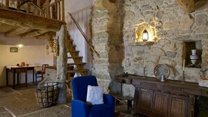 A rustic stone interior with a wooden staircase, a blue armchair, a fireplace, and a stone wall with a niche. - Aldeia da Mata Pequena (Mafra)